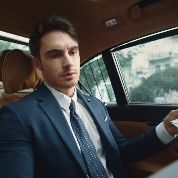 Volvo V60 Classe-Affaires VTC Haute-Savoie Homme en costume assis dans une voiture, regard pensif, vue sur la route.