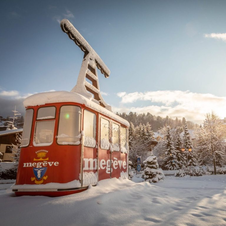 VTC, Taxi, Chauffeur privé Classe-Affaires VTC en Haute-Savoie, Chamonix, Genève et Annecy. Cabine de téléphérique rouge de Megève recouverte de neige, entourée de sapins sous un ciel ensoleillé.